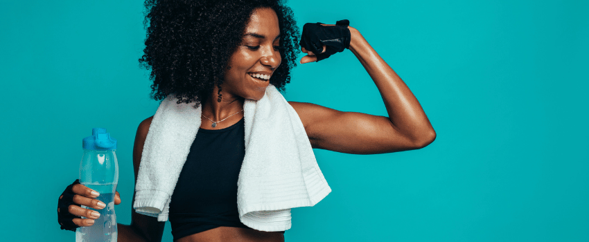 A female teacher in a sports bra and towel, holding a water bottle, is ready for a workout class purchased with fitness teacher discounts.
