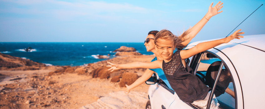 A teacher and her daughter joyfully extend their arms out the car windows, embracing the moment together on a trip made possible by using travel teacher discounts.
